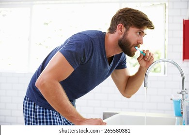 Man In Pajamas Brushing Teeth In Bathroom