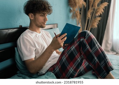 Man in pajamas sitting on his bed writing notes in journal. Copy space