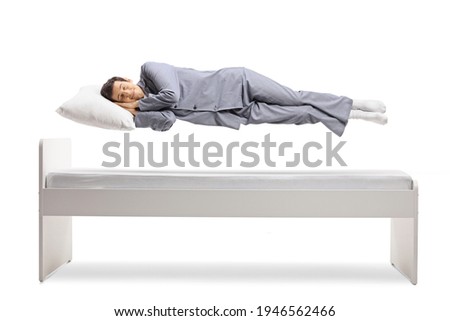 Man in pajamas sleeping and floating above a bed isolated on white background