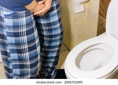 A Man In Pajamas Standing Over The Toilet And Holding His Stomach. The Concept Of Prostate And Urination Problems 