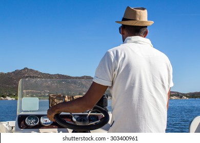 A Man With A Panama Hat Driving A Boat Near The Coast