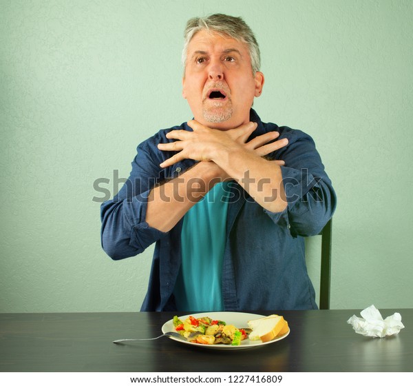 A man is panicking and is in trouble as he\
chokes on food and is making the official international sign for\
\