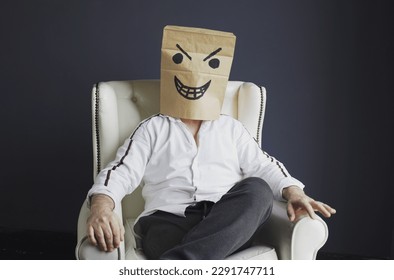 A man with a paper bag on his head, with a drawn angry smiley face, sits in a white chair. Emotions and gestures. - Powered by Shutterstock