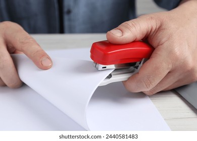 Man with papers using stapler at white table, closeup
