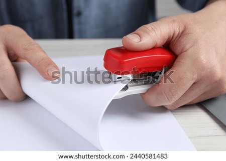Man with papers using stapler at white table, closeup