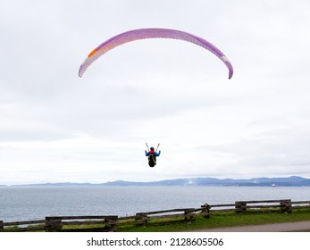 Man paragliding just above a coastline park during an overcast day, Victoria, British Columbia, Canada
