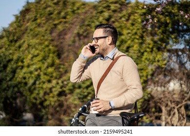 A Man In Park With Bicycle Talking On The Phone And Enjoying Coffee To Go.