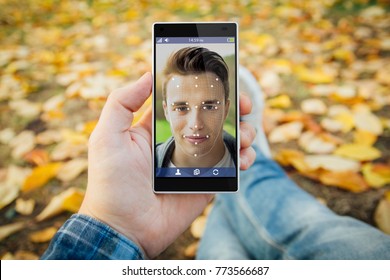 Man In The Park Unlocking Smartphone With Facial Recognition. All Screen Graphics Are Made Up.