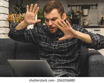 A Man Participates In An Online Meeting - A Web Conference Staying At Home. Man Looks At The Screen Of The Laptop And Actively Gesticulates With His Hands.