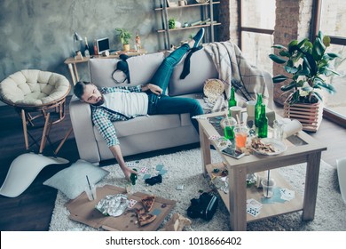 Man, Party Maker Having Hangover After Stag Party, Sleeping On Sofa, Holding Bottle Of Beer With Chaos In The Messy Living Room After Night Party