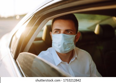 Man Passenger In Protective Sterile Medical Mask In The Taxi Car During An Epidemic In Quarantine City. Health Protection, Safety And Pandemic Concept. Covid - 19.