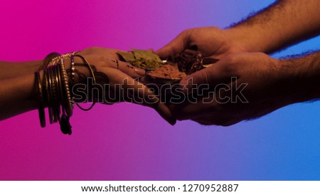 Man passes a plate of spices to indian woman with many bracelets and mehendi on her hands, isolated on bright background. Stock. Man giving set of spices in a plate to woman, indian bazar concept.
