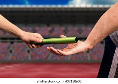 Man passing the baton to partner on track against athletic field on a stadium