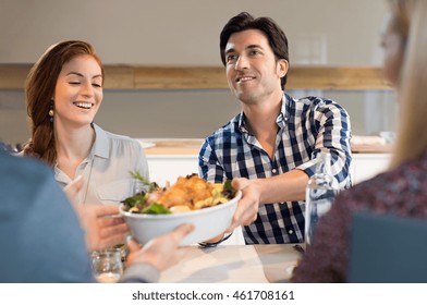 Man Passing Food Bowl With Roasted Chicken To His Friend. Happy Smiling Man Eating With His Friends At Home.Young Friend Socializing After A Long Time.