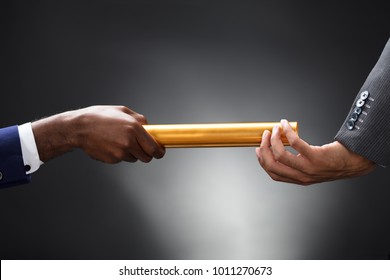 Man Passing The Golden Baton To His Partner On Gray Background