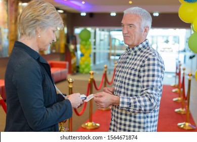 Man passing ticket to woman in lobby of theatre