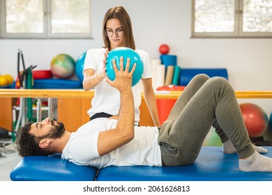 Man patient and female physiotherapist exercising with a small pilates ball with both hands, in front of his chest.