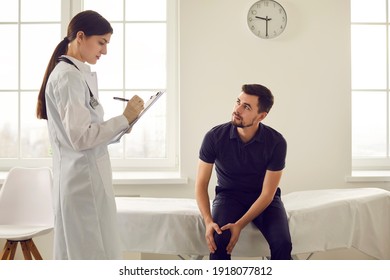 Man Patient Showing Pain In Knee During Visit With Young Woman Doctor Therapist In Medical Clinic Or Rehabilitation Center Office. Visiting Doctor And Healthcare Support Concept