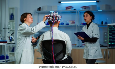 Man Patient Wearing Performant Eeg Headset Scanning Brain Electrical Activity In Neurological Research Laboratory While Medical Researcher Controlling It, Examining Nervous System, Nurse Taking Notes