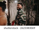 A man in a patterned jacket smiling during an outdoor nighttime party setting. Fairy lights and natural surroundings create a joyful and celebratory atmosphere, capturing warmth and camaraderie.