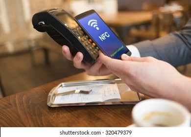 Man Paying With NFC Technology On Mobile Phone, In Restaurant, Bar, Cafe