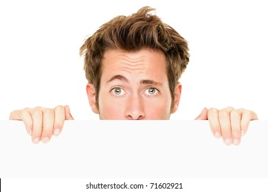 Man peaking showing blank empty white billboard sign surprised. Closeup of young man peeping over white banner edge. Isolated on white background.