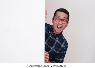 A man peeking from behind blank billboard showing amazed expression - Powered by Shutterstock