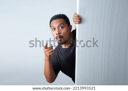 man peeking behind wall while pointing finger