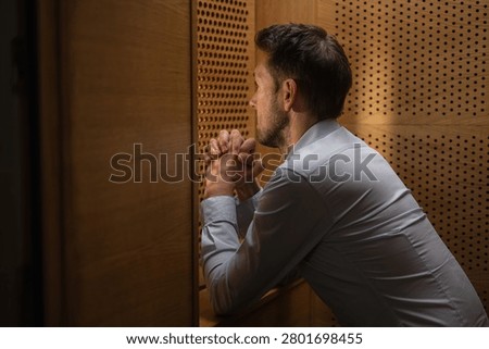 Man penitent, in a confession booth, confessing sins to a priest to receive absolution and spiritual healing. Faith concept.