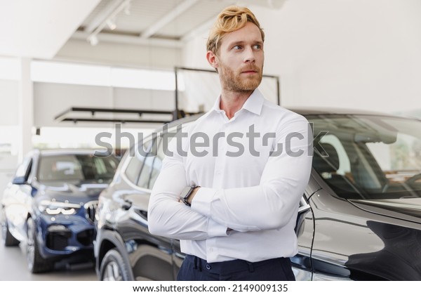 Man pensive serious customer male buyer client\
wear white shirt hold hand crossed folded choose auto want buy new\
car automobile in showroom vehicle dealership store motor show\
indoor Sales concept.