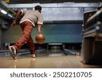 Man performing a bowling release in modern bowling alley with focused posture. Background features lanes and equipment creating dynamic atmosphere