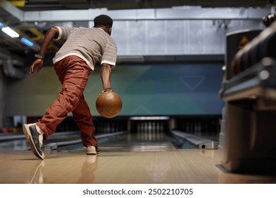 Man performing a bowling release in modern bowling alley with focused posture. Background features lanes and equipment creating dynamic atmosphere