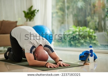 Man performing child pose and doing yoga at home