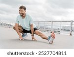 A Man Performing a Dynamic Stretching Exercise Outdoors on a Cloudy Day Near a Waterfront