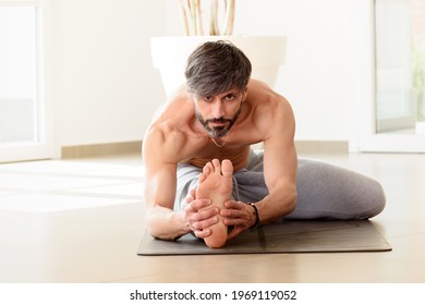 Man Performing A Janu Sirsana Head To Knee Yoga Pose To Stretch The Spine, Shoulders, Hamstrings, And Groin In A Health And Fitness Concept In A High Key Gym With Copyspace