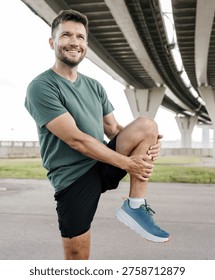 Man performing a leg stretch exercise under a bridge during his outdoor workout
