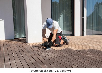 Man performing maintenance on home exterior wooden deck - Shutterstock ID 2379869995