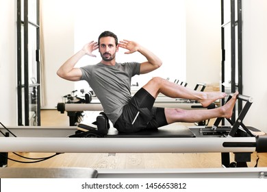Man performing a pilates single leg stretch exercise on a reformer bed in a gym twisting to face the camera to stretch and tone the abdominal muscles