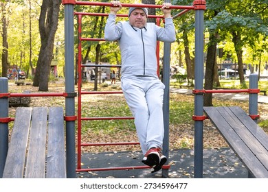 Man performing pull ups on horizontal bar during outdoor training in park. Concept of physical activity, persistence and fitness goals