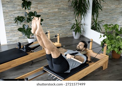 A man performs an advanced Pilates exercise on a reformer machine to enhance flexibility and strength.