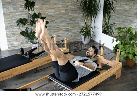A man performs an advanced Pilates exercise on a reformer machine to enhance flexibility and strength.