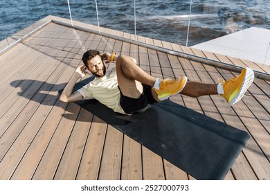 A Man Performs Bicycle Crunches on a Yoga Mat by the Water on a Sunny Day, Promoting Fitness and Outdoor Exercise - Powered by Shutterstock