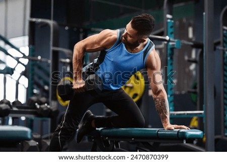 A man performs a dumbbell row exercise while kneeling on a weight bench in a gym.