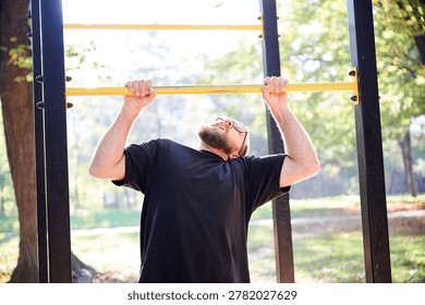 Man performs pull up on horizontal bar at outdoor gym in park. Active fitness scene for strength training, calisthenics, healthy lifestyle, sports motivation, or workout promotion