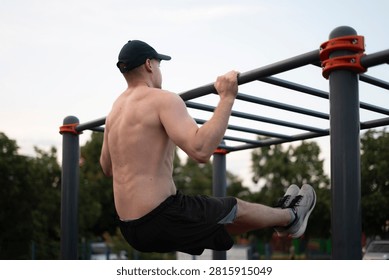 A man performs pull-ups on a bar in an outdoor gym as the sun sets in a park setting.