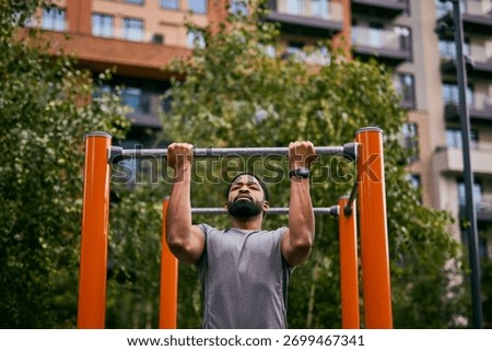 A man performs pull-ups on an outdoor gym structure in an urban park, showcasing fitness and determination.