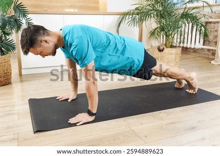 Man performs push-ups on a yoga mat in a bright, modern indoor space surrounded by plants
