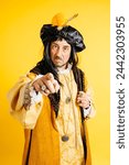 A man in a period costume resembling Christopher Columbus points forward authoritatively, with elaborate garb set against a bold yellow background.