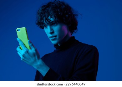 Man with phone in hand looking at smartphone screen, portrait dark blue background, neon light, style and trends, mixed light, men's fashion, copy place