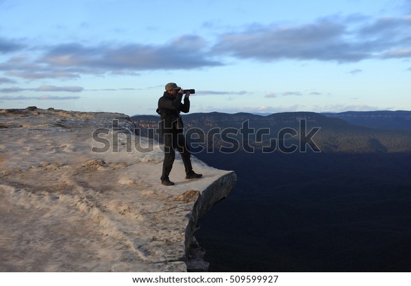 Man photographer stands on a cliff and\
photographing the landscape from Lincoln Rock Lookout at sunrise in\
the Blue Mountains National Park in the Blue Mountains region of\
New South Wales, Australia